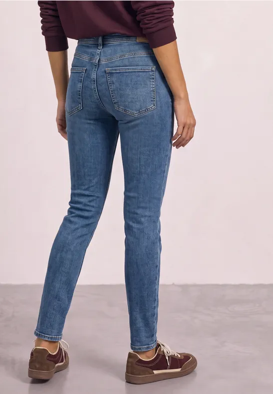 Person von hinten in blauen Skinny-Jeans und braunen Sneakern.
