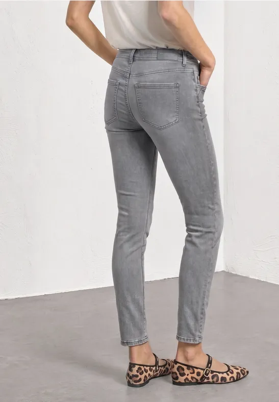Person von hinten in grauen Jeans und Leo-Ballerinas vor weißem Hintergrund.