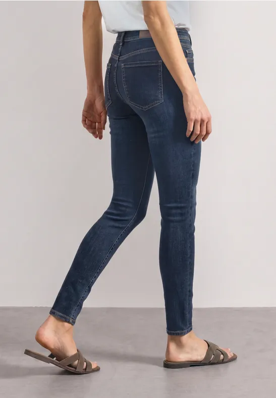 Dame trägt dunkelblaue Skinny-Jeans und flache braune Sandalen.