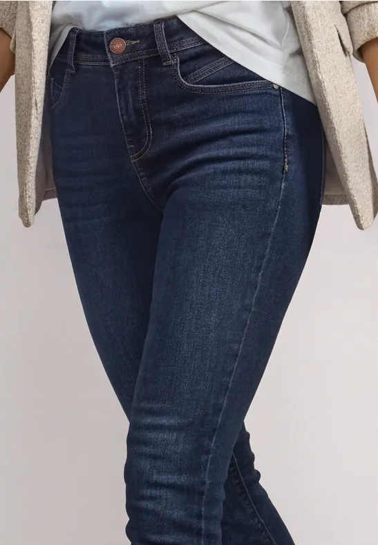 Frau in dunkelblauen Skinny-Jeans mit weißem Shirt und beigem Blazer, Fokus auf Hüfte und Beine.
