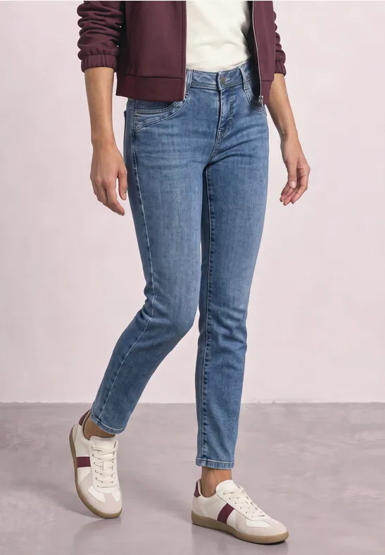 Person trägt blaue Jeans, weiße Sneakers und ein bordeauxfarbenes Oberteil.