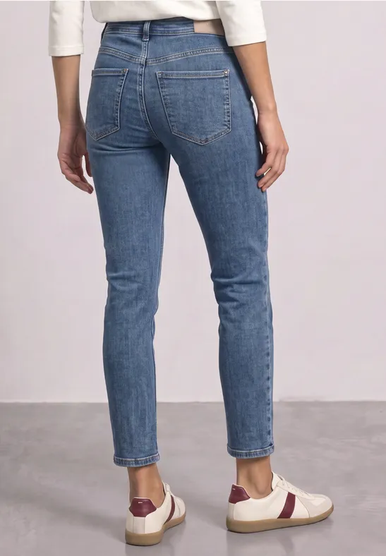 Person von hinten in schmal geschnittenen blauen Jeans und weißen Sneakers mit roten Details.