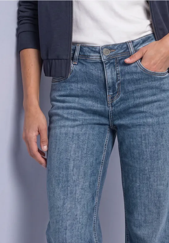 Frau trägt blaue Jeans, weißes T-Shirt und dunkle Jacke, Hand in Hosentasche