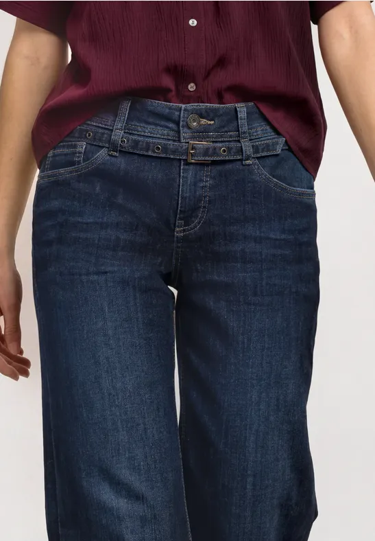 Frau trägt dunkelblaue High-Waist-Jeans mit doppeltem Taillengürtel und kastigem kurzärmeligem weinroten Oberteil.