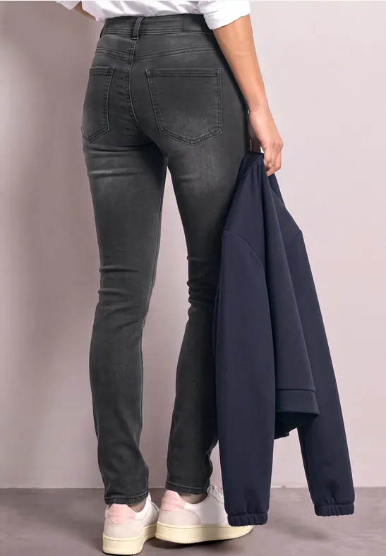 Person trägt enge, schwarze Jeans und weiße Sneaker, hält eine dunkelblaue Jacke in der Hand.