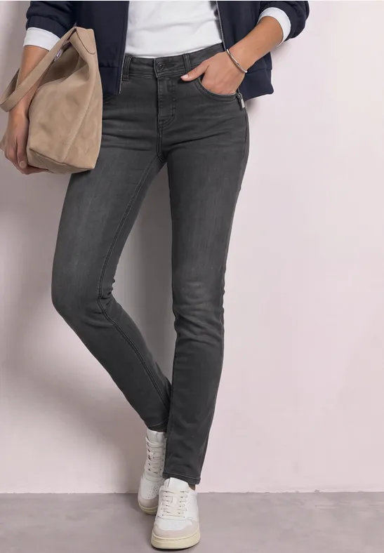 Frau in grauen Skinny-Jeans, weißen Sneakern, trägt eine beige Stofftasche.