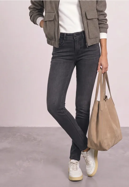 Person trägt schwarze Skinny Jeans, weiße Sneaker, olivgrüne Bomberjacke, weißes T-Shirt und eine beige Tasche.