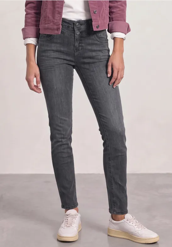 Eine Person trägt dunkelgraue, eng anliegende Jeans und weiße Sneaker.