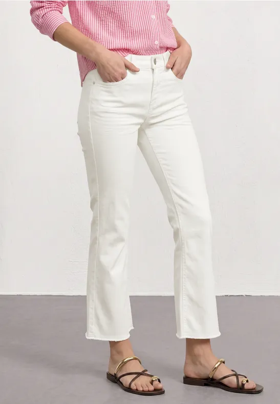 Een persoon draagt witte flared jeans, zwarte sandalen en een roze bovenstuk.