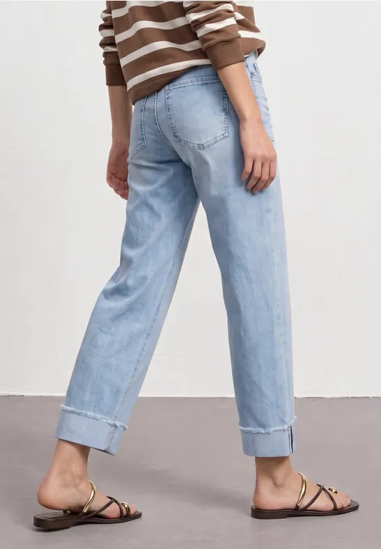 Person in hellblauen, aufgekrempelten Jeans, gestreiftem Pullover und flachen Sandalen.