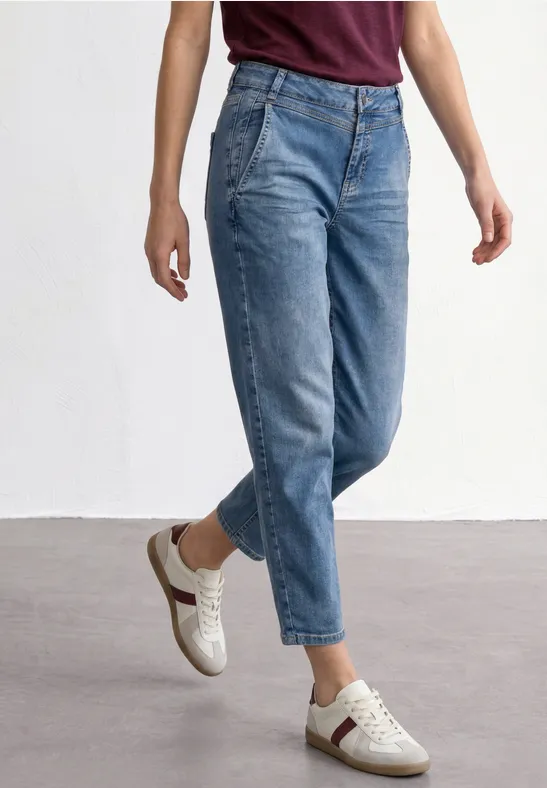 Een persoon draagt lichtblauwe hoog getailleerde jeans en witte sneakers voor een witte achtergrond.