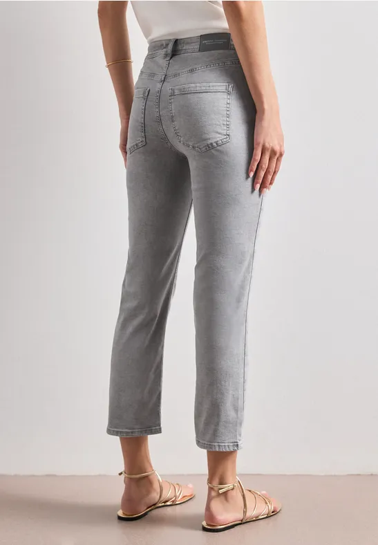 Rückansicht einer Person in hochgeschnittenen, grauen, knöchellangen Jeans mit geradem Bein und flachen Sandalen.