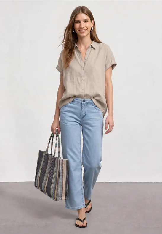 Frau in beiger Bluse und Jeans mit schwarzen Flip-Flops und gestreifter Tasche, entspannt unterwegs.