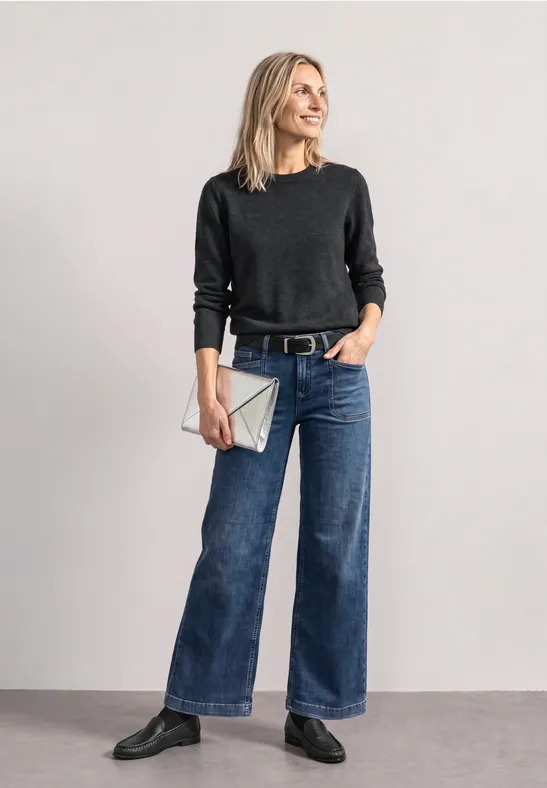 Eine Frau in schwarzem Pullover, weiten Jeans und schwarzen Stiefeln mit silberner Clutch.