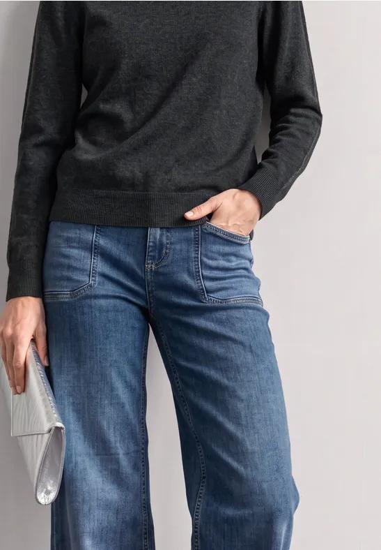 Person trägt dunklen Pullover, blaue Jeans und hält eine silberne Clutch.