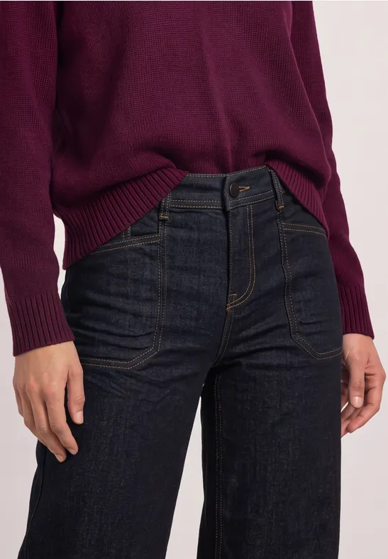 Eine Person trägt einen bordeauxfarbenen Pullover und dunkle Jeans.