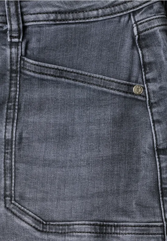 Nahaufnahme einer dunklen Jeanshose: schräge Münztasche mit Metallknopf und sichtbaren Nähten.
