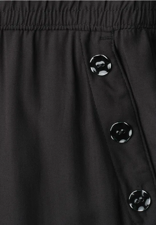 Schwarze Hose mit elastischem Bund und seitlicher Knopfleiste mit drei Knöpfen.