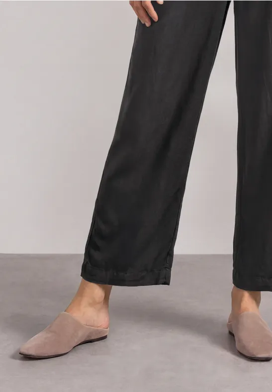 Person trägt schwarze weite Hose und graue Mules auf grauem Boden.