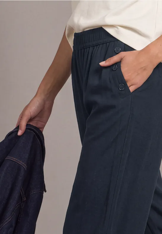 Person trägt dunkelblaue Hose, Hand steckt in Tasche, hält Jeansjacke in der Hand.