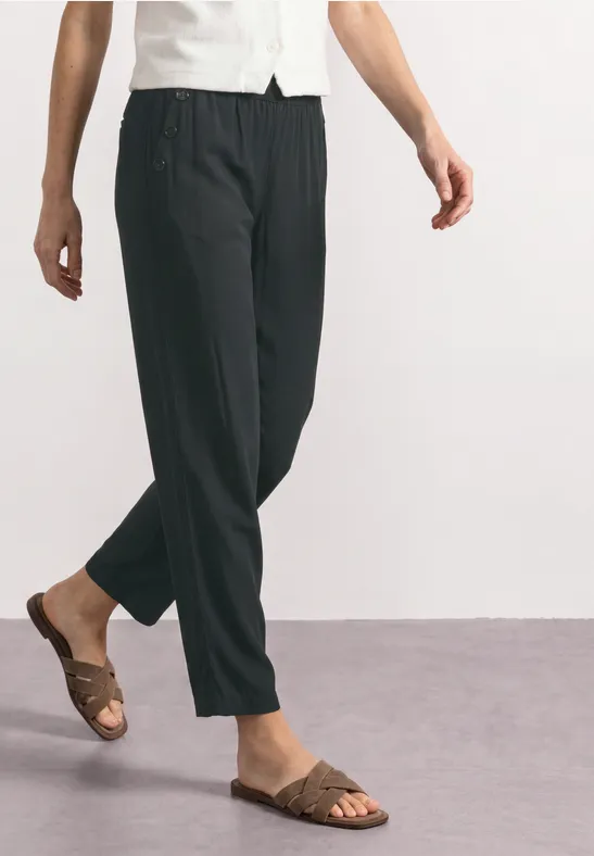 Eine Person trägt schwarze, locker sitzende Hosen und braune Sandalen auf grauem Boden.