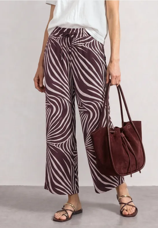 Modieuze look: wijde zebraprintbroek, platte sandalen en grote bordeauxrode suèdetas.