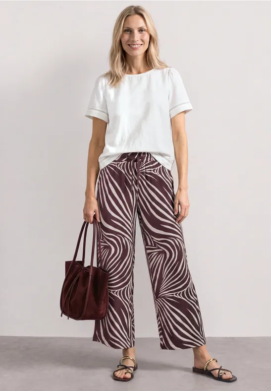 Persoon met wit T-shirt, wijde broek met zebraprint, sandalen en een bruine tas.