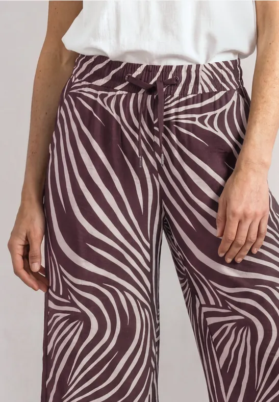 Close-up van persoon in witte top en wijde bruine broek met wit zebra-patroon.