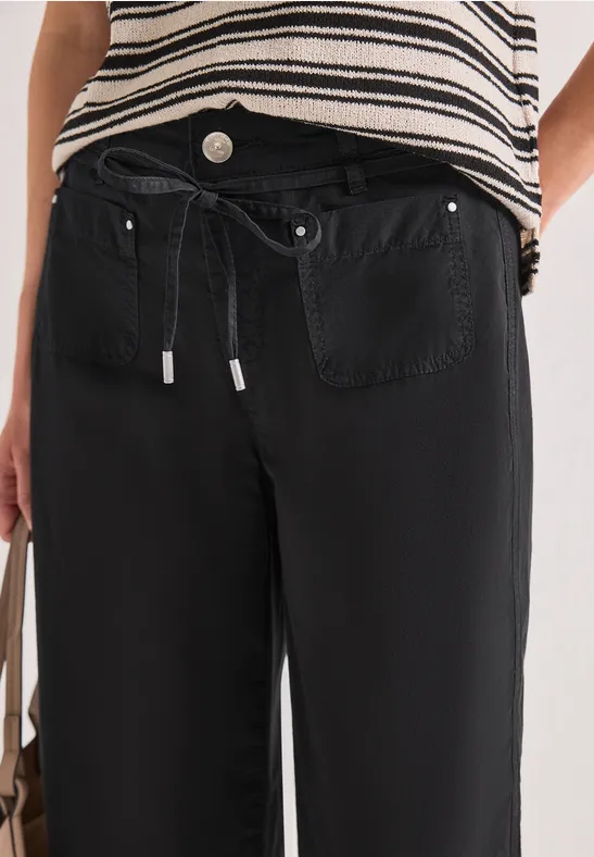 Person trägt gestreiftes Oberteil und schwarze, lässige Hose mit Tunnelzugbund und aufgesetzten Taschen.