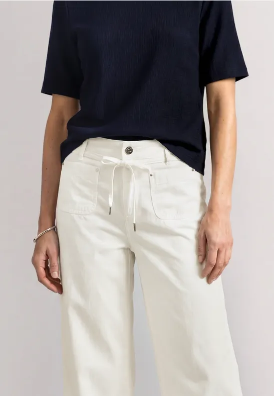 Frau in schwarzem Kurzarmshirt und weißen, weiten Hosen.
