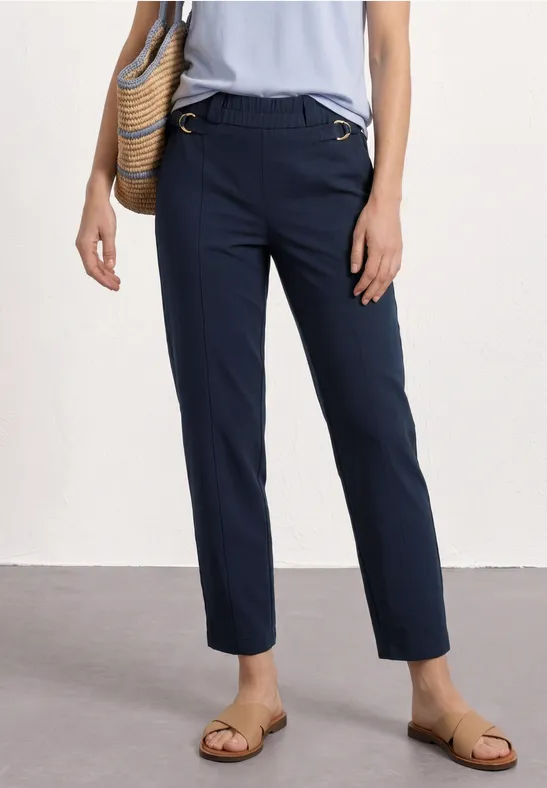 Navyblauwe, recht gesneden broek, platte sandalen en gevlochten tas aan de heup.