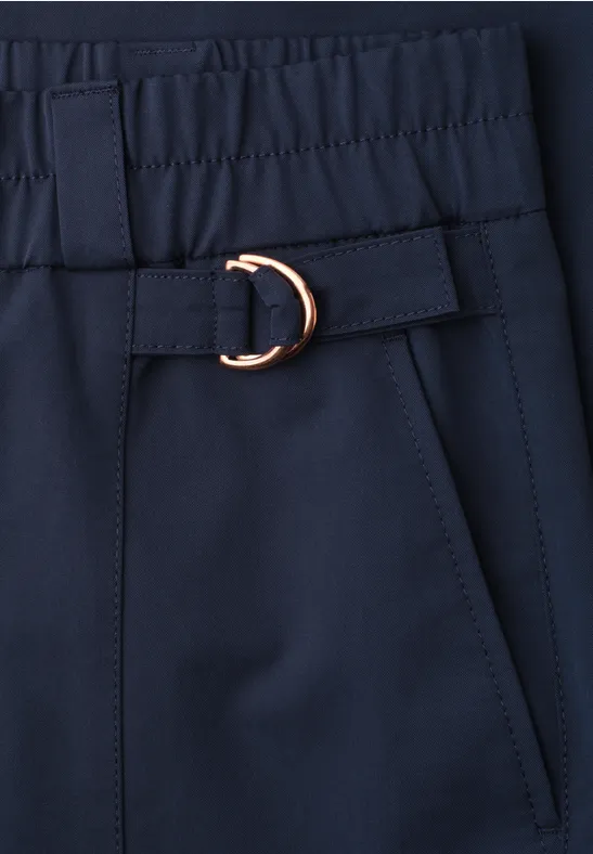 Close-up van een donkerblauw kledingstuk met elastische taille, zijzak en gouden D-ring