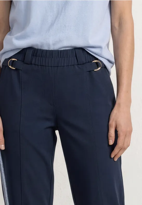 Donkerblauwe broek met elastische taille en zilverkleurige ringen, gecombineerd met lichtblauw shirt.