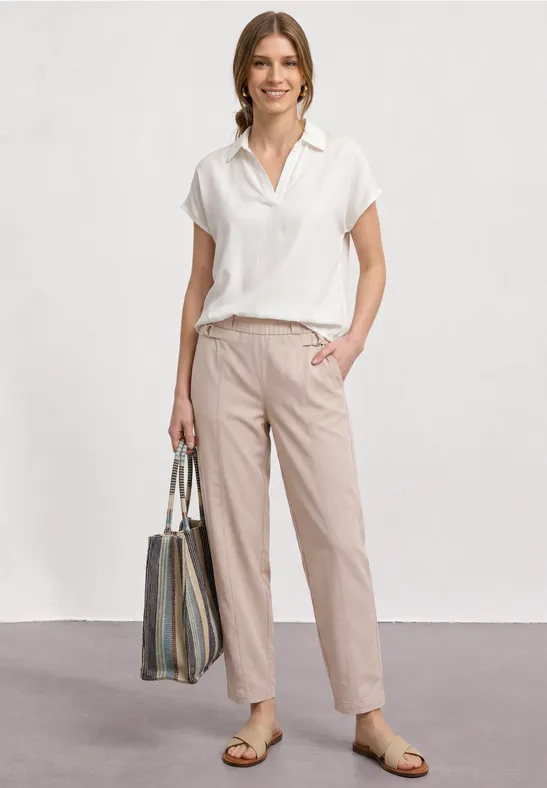 Iemand draagt een wit overhemd met korte mouwen, een beige broek, sandalen en een grote gestreepte tas.