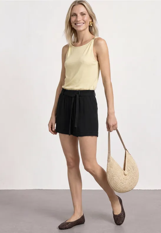 Frau in gelbem Top, schwarzen Shorts und großer Strohtasche.
