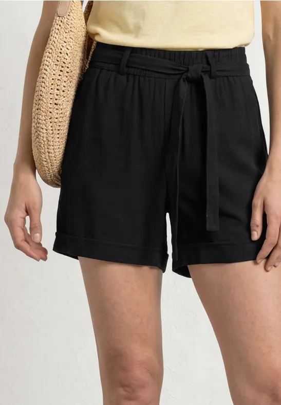 Schwarze, lockere Shorts mit Taillengürtel, dazu gelbes Top und Strohtasche.
