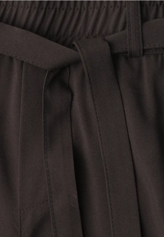 Detailaufnahme eines Hosenbunds mit elastischem Gummizug und Stoffgürtel in dunkler Farbe.