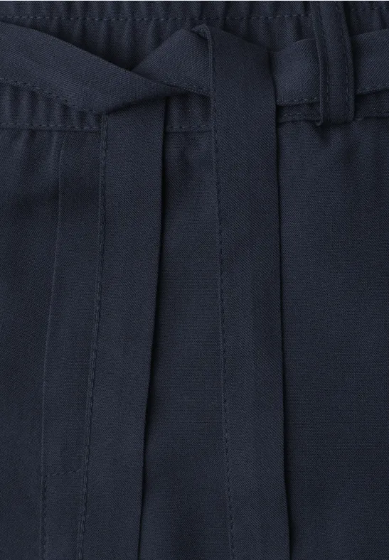 Close-up van een donkerblauwe broek met elastische taille en los gestrikte stoffen ceintuur.