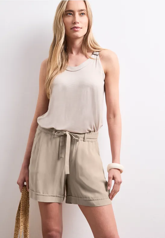 Vrouw in beige tanktop en short met een strozak voor een lichte achtergrond.