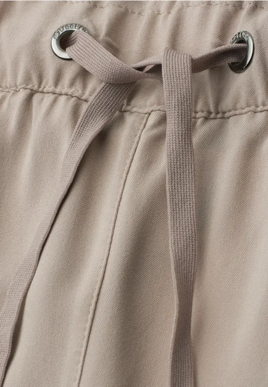 Nahaufnahme einer beigefarbenen Hose mit Tunnelzug und Metallösen am Bund.
