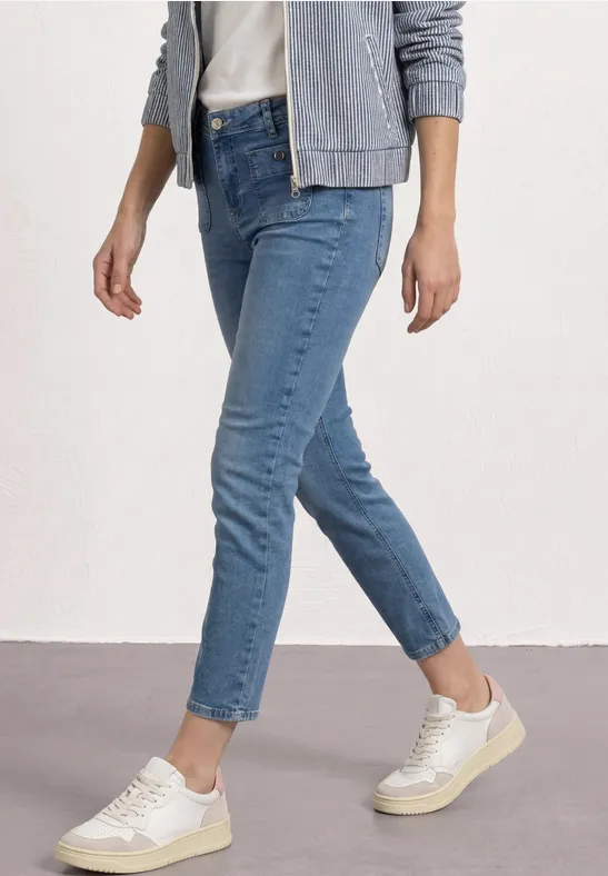 Person trägt blaue knöchellange Jeans, weiße Sneaker und graue Jacke.