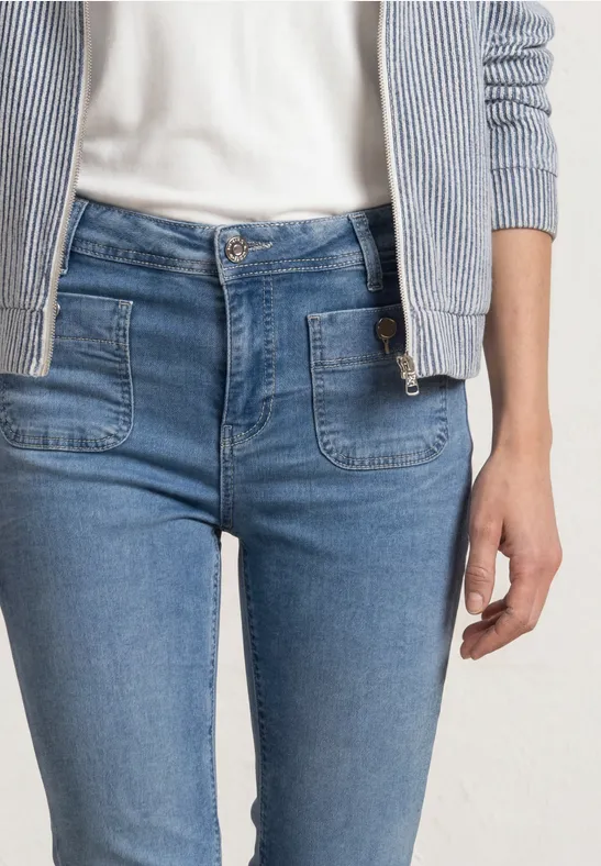 Frau in engen mittelblauen Jeans mit aufgesetzten Taschen, weißem Shirt und gestreifter Jacke.