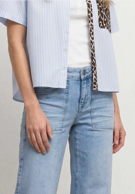 Une personne porte un jean bleu clair et une chemise à rayures manches courtes sur un top blanc.