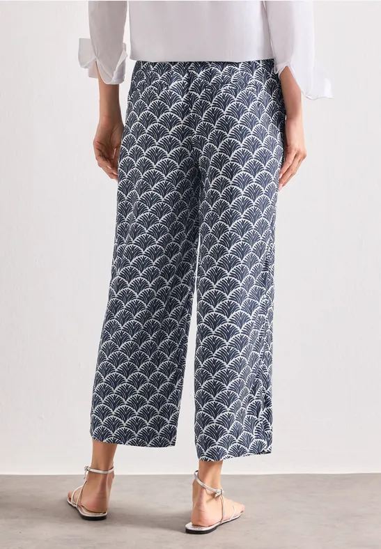Rückansicht einer Person in weiten, knöchellangen blau-weiß gemusterten Culottes, weißem Top und Sandalen.