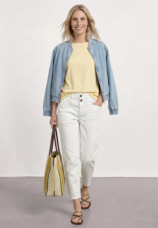 Frau im lässigen Outfit: hellblaues Jackett, gelbes Shirt, weiße Hose, Sandalen und gelbe Tasche.