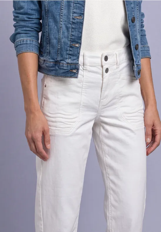 Eine Frau trägt weiße High-Waist-Jeans mit Knopfleiste und eine blaue Jeansjacke.