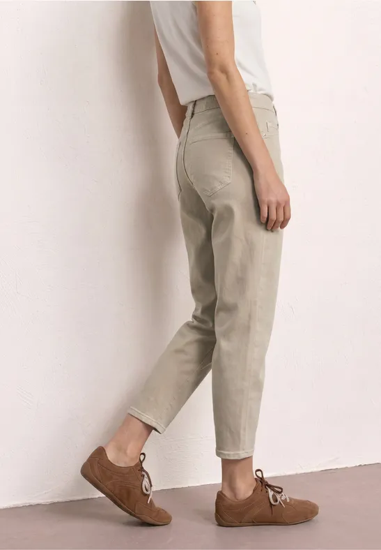 Unterkörper einer Person mit beigen, lässigen Hosen und braunen Schnürschuhen vor neutralem Hintergrund.