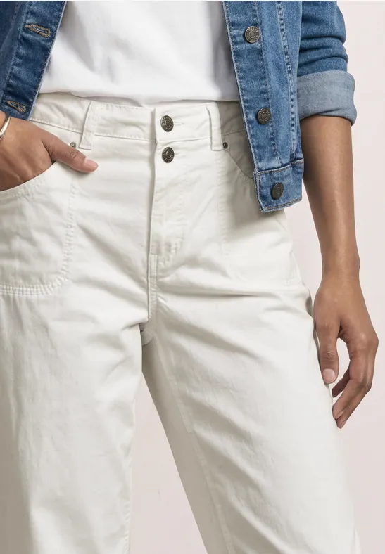 Person trägt helle Jeans mit hoher Taille und Doppelknopf, kombiniert mit weißem Shirt und Jeansjacke.