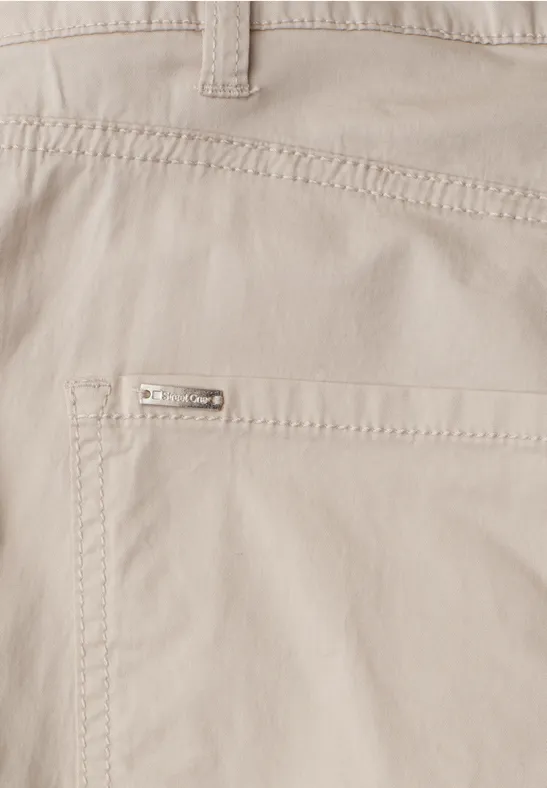 Close-up einer hellbeigen Hose mit aufgesetzter Tasche und kleinem Metalllogo.