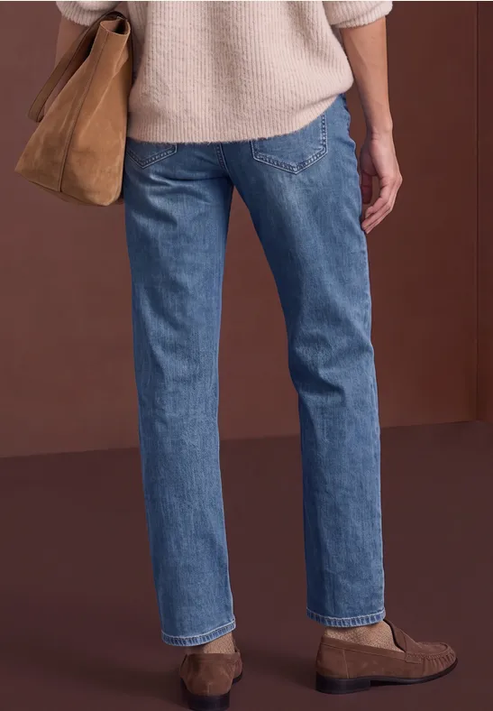 Vue de dos d’une personne portant un pull clair, un jean bleu, un sac et des chaussures bruns.